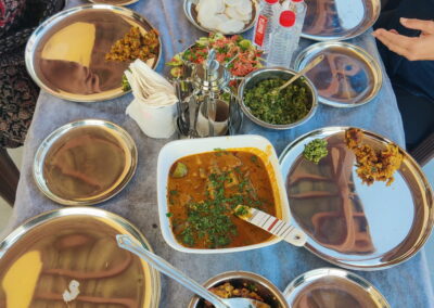 Table set for a meal with multiple metal dishes, curries, greens, onions, and bottled water on a blue tablecloth. - aamod villa  holiday home